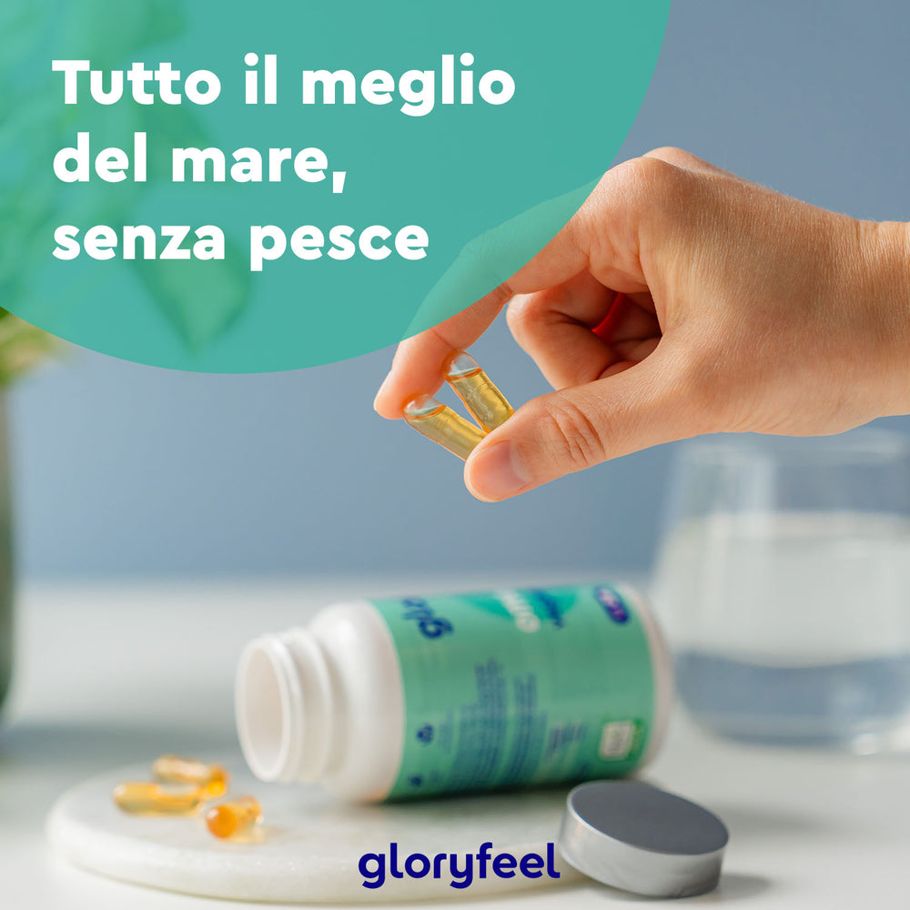 Una mano tiene una capsula vicino a una bottiglia di integratori Omega 3 Vegan - Olio di alghe su un tavolo, con un testo in italiano che dice &quot;Tutto il meglio del mare, senza pesce&quot; e un marchio etichettato come Gloryfeel Italia.