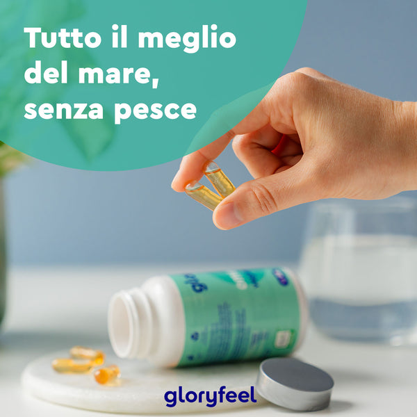 Una mano tiene una capsula vicino a una bottiglia di integratori Omega 3 Vegan - Olio di alghe su un tavolo, con un testo in italiano che dice &quot;Tutto il meglio del mare, senza pesce&quot; e un marchio etichettato come Gloryfeel Italia.