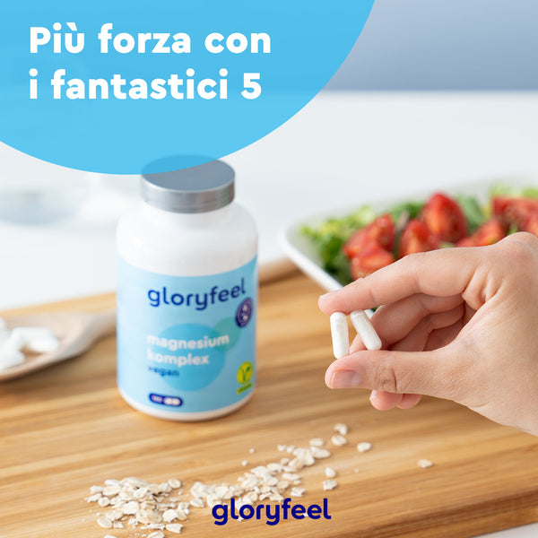 Una mano tiene due capsule vicino a una bottiglia di &quot;gloryfeel Italia Magnesio Complex&quot; su un tavolo di legno, circondata da avena e insalata. Il testo italiano recita: &quot;Più forza con i fantastici 5&quot;. Questa scena equilibrata fonde l&