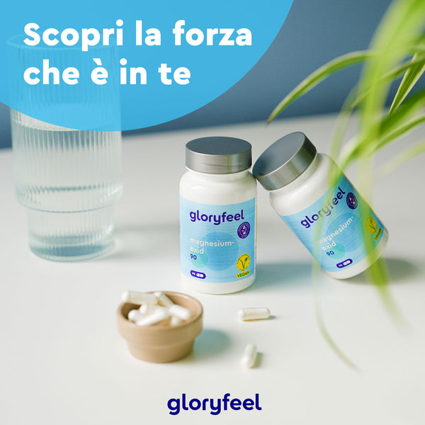 Due flaconi di integratori in capsule Magnesio Ossido 90 di gloryfeel Italia e una piccola ciotola di capsule sono appoggiati su un tavolo con un bicchiere d&