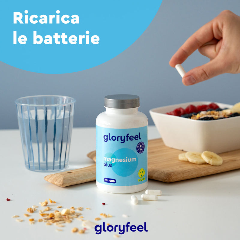 Una mano tiene una pillola su una tavola di legno con una bottiglia di Magnesio Plus 180 di GloryFeel GmbH Italia, un bicchiere d&